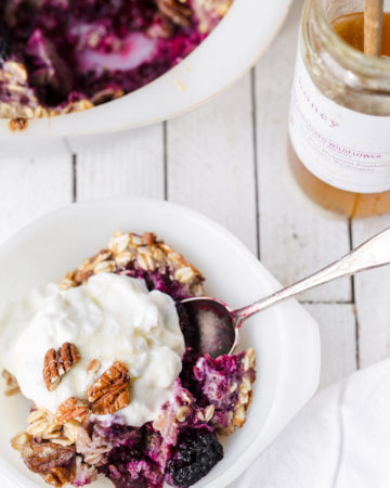 Scoop of blackberry baked oatmeal with greek yogurt and honey on the table